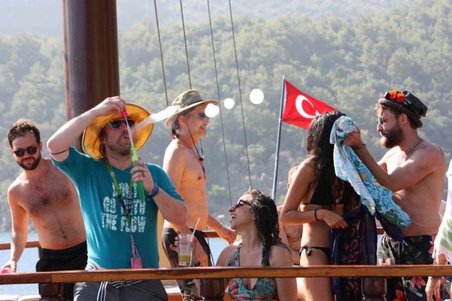 A group laughing and blowing bubbles on a gulet, a Turkish flag behind them.