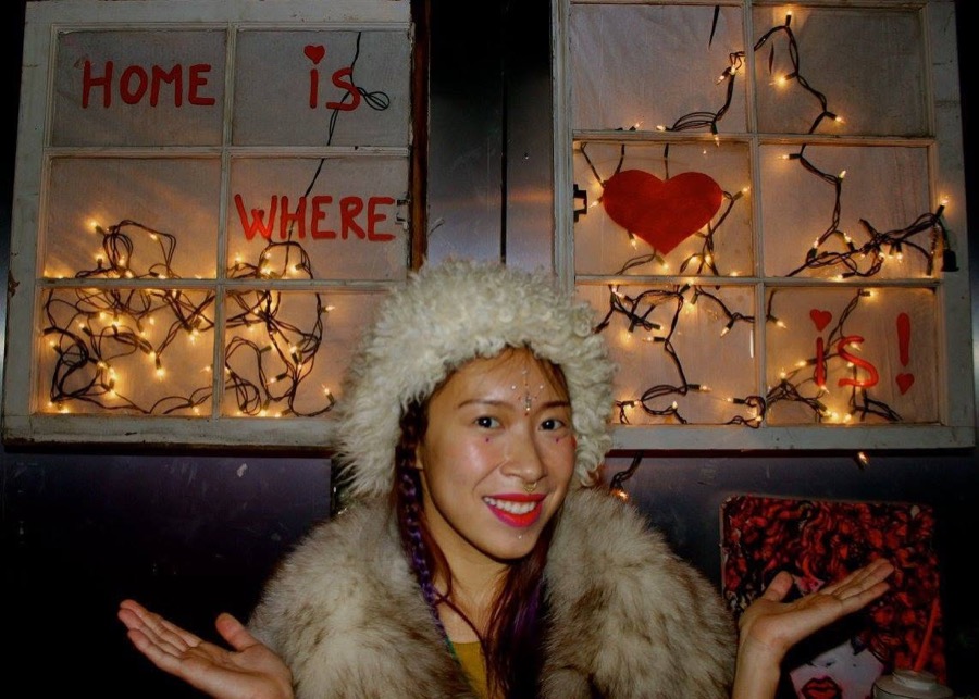 A window strung with fairy lights, painted with the words HOME IS WHERE HEART IS, and a member smiling in front of it.