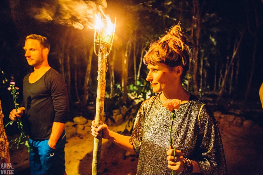 Two members walking through the jungle at night, one carrying a lit torch and a flower.